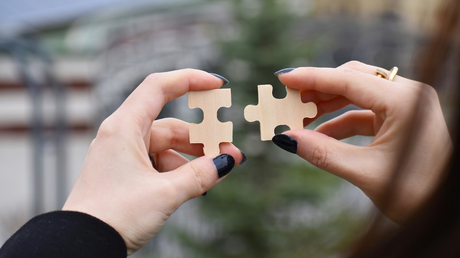 Two hands holding wooden puzzle pieces about to connect, representing the process of recovering failed payments and reconnecting with customers through dunning best practices.